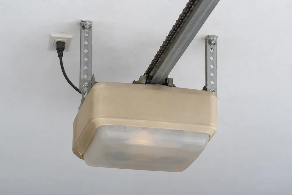 Older beige chain-drive garage door opener with a cloudy light lens hanging from ceiling straps